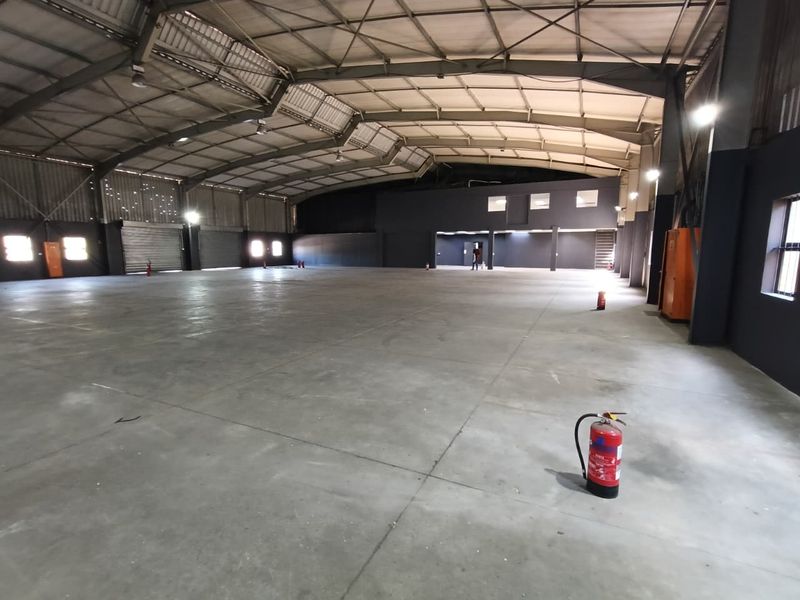 Spacious industrial warehouse featuring concrete flooring, high-clearance steel portal frame construction, roller shutter access, and functional industrial lighting throughout.