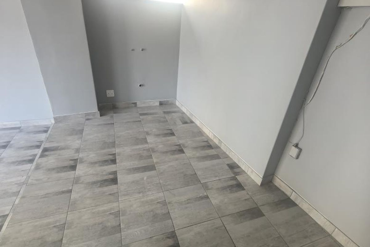 An empty, neutral-toned room featuring grey wood-look floor tiles, crown molding, and wall-mounted electrical and plumbing points, suitable for various business uses.