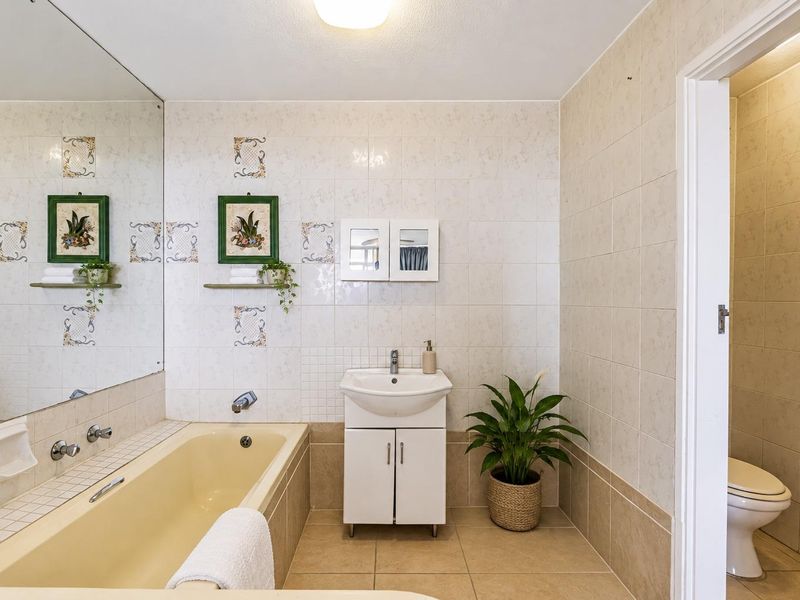 A functional bathroom featuring a built-in bathtub, vanity cabinet, and separate toilet area with neutral ceramic tiling throughout.