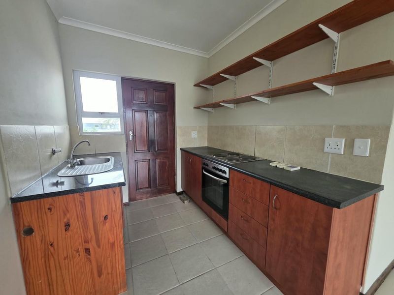 Functional kitchen featuring wooden cabinetry, granite countertops, built-in oven and hob, tiled backsplash, and open shelving for storage.