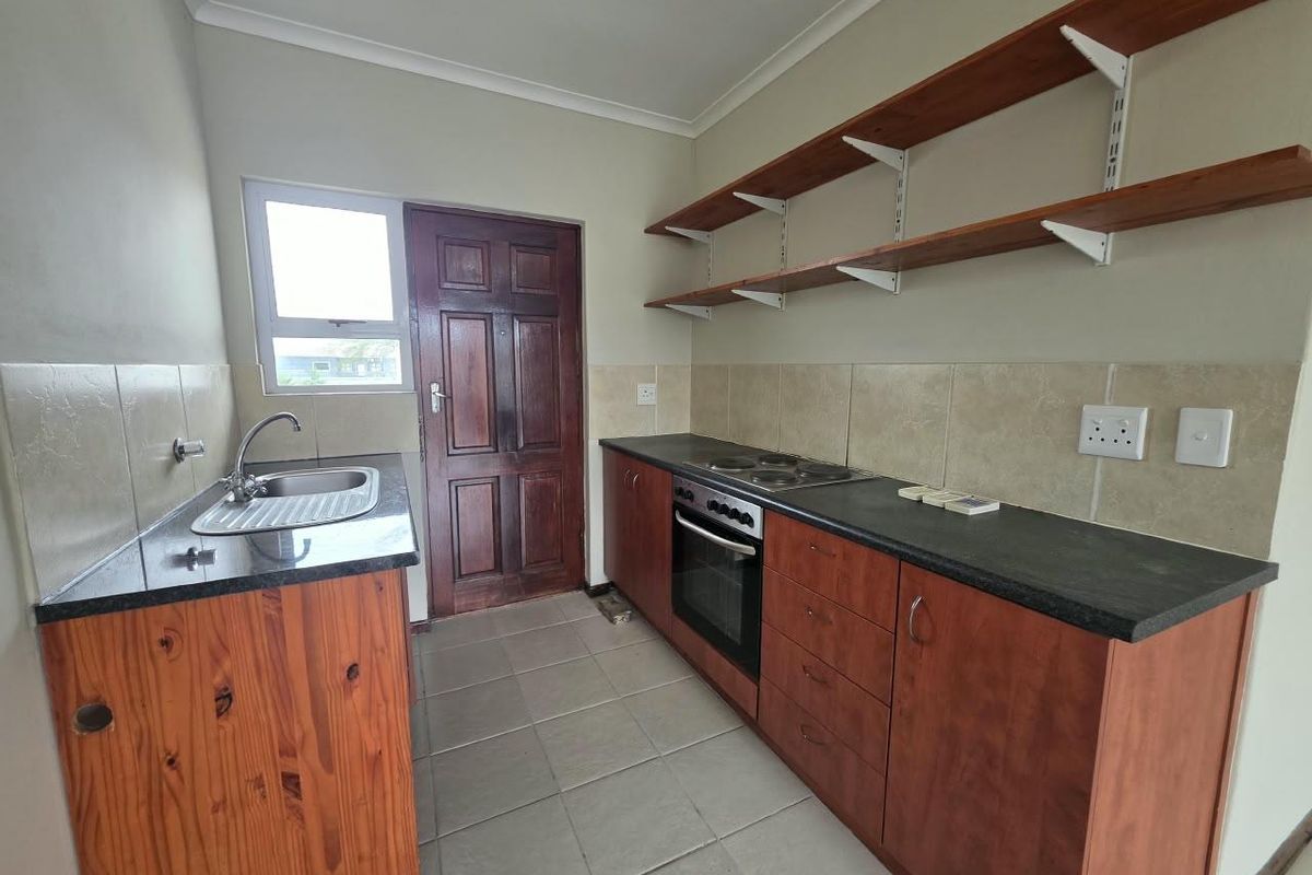 Functional kitchen featuring wooden cabinetry, granite countertops, built-in oven and hob, tiled backsplash, and open shelving for storage.