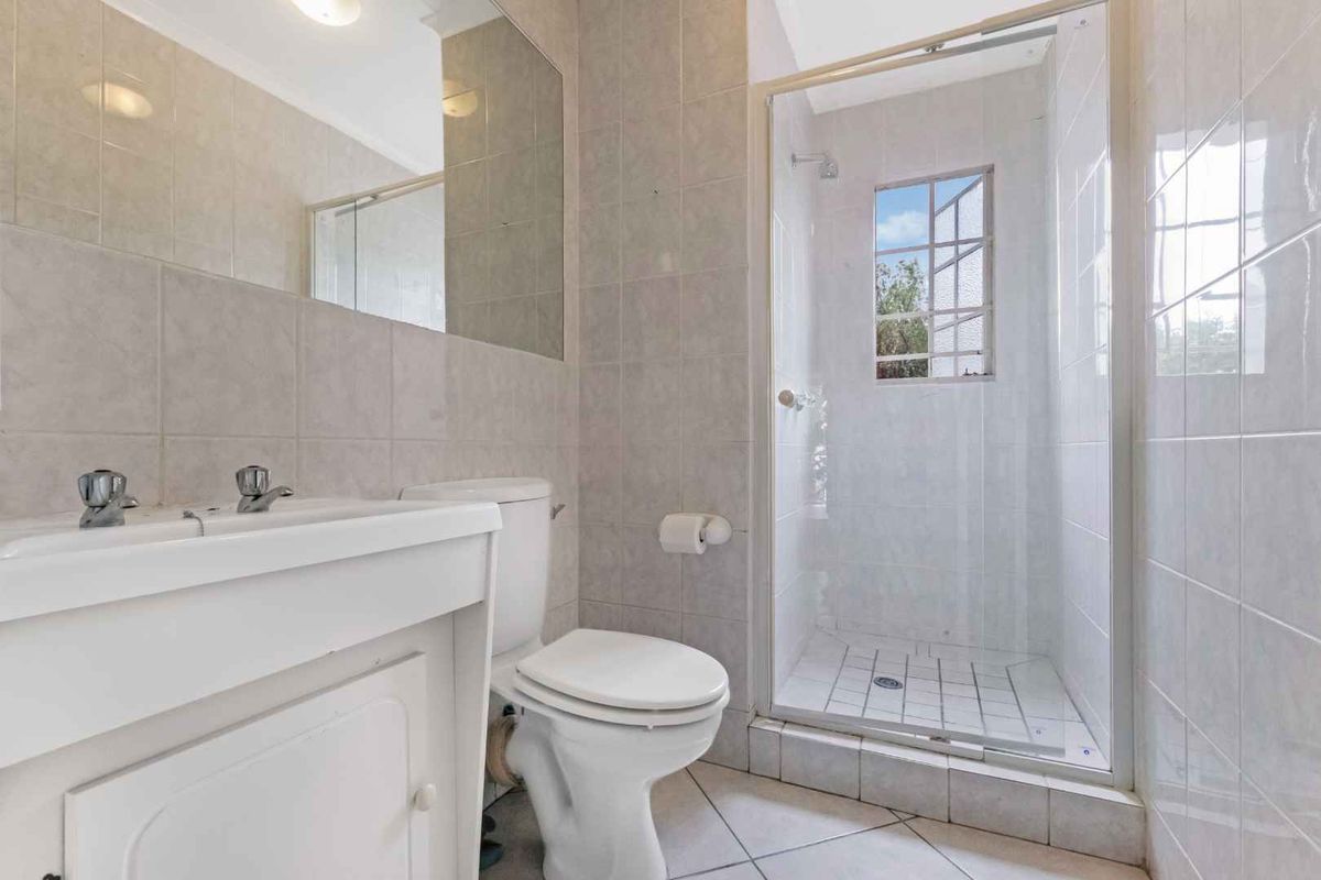 A functional bathroom featuring a tiled shower enclosure, a vanity basin with a wall-mounted mirror, and a standard toilet.
