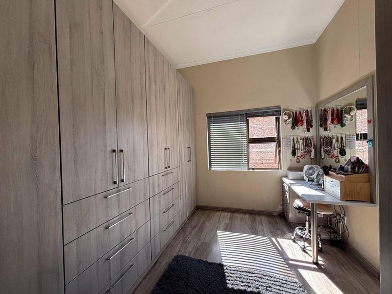 A well-maintained bedroom featuring extensive floor-to-ceiling built-in cupboards, modern laminate flooring, and a built-in vanity area with natural light.