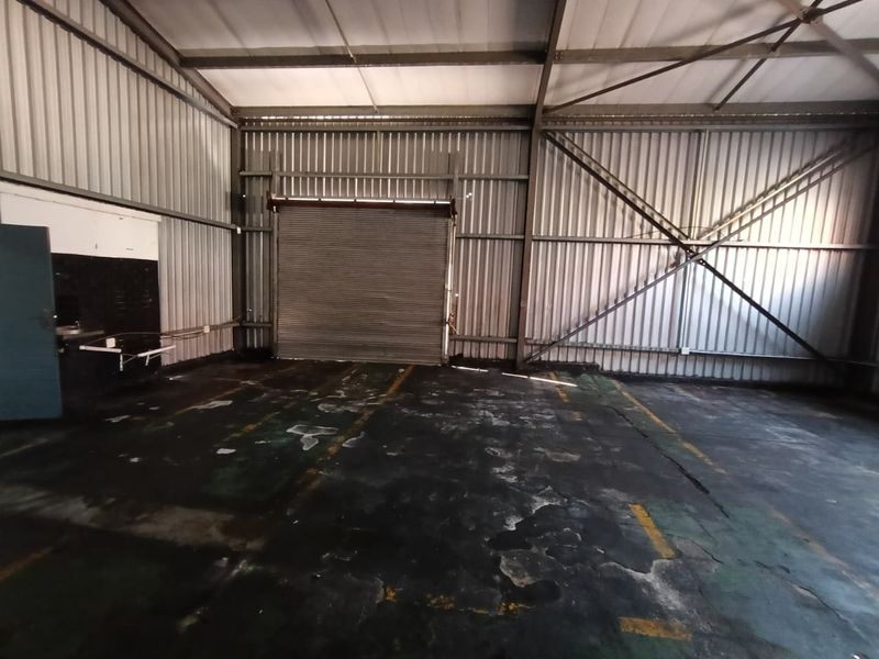 Spacious industrial utility area featuring a high-clearance roller shutter door, exposed steel frame construction, and durable concrete flooring suitable for storage or workshop use.