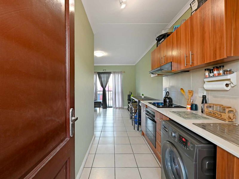 Open-plan kitchen and living area featuring tiled flooring, built-in wooden cabinetry, and a sliding door leading to a balcony.