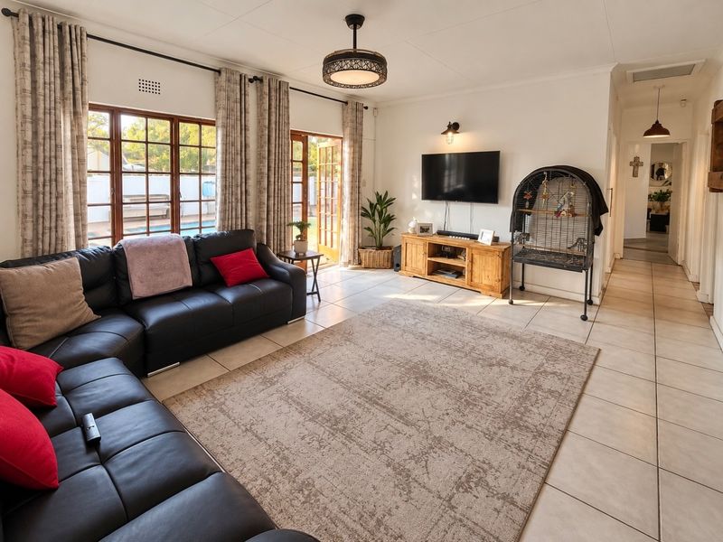 A bright and spacious living room featuring tiled flooring, large wooden-framed glass doors providing natural light, and direct access to the outdoor pool area.
