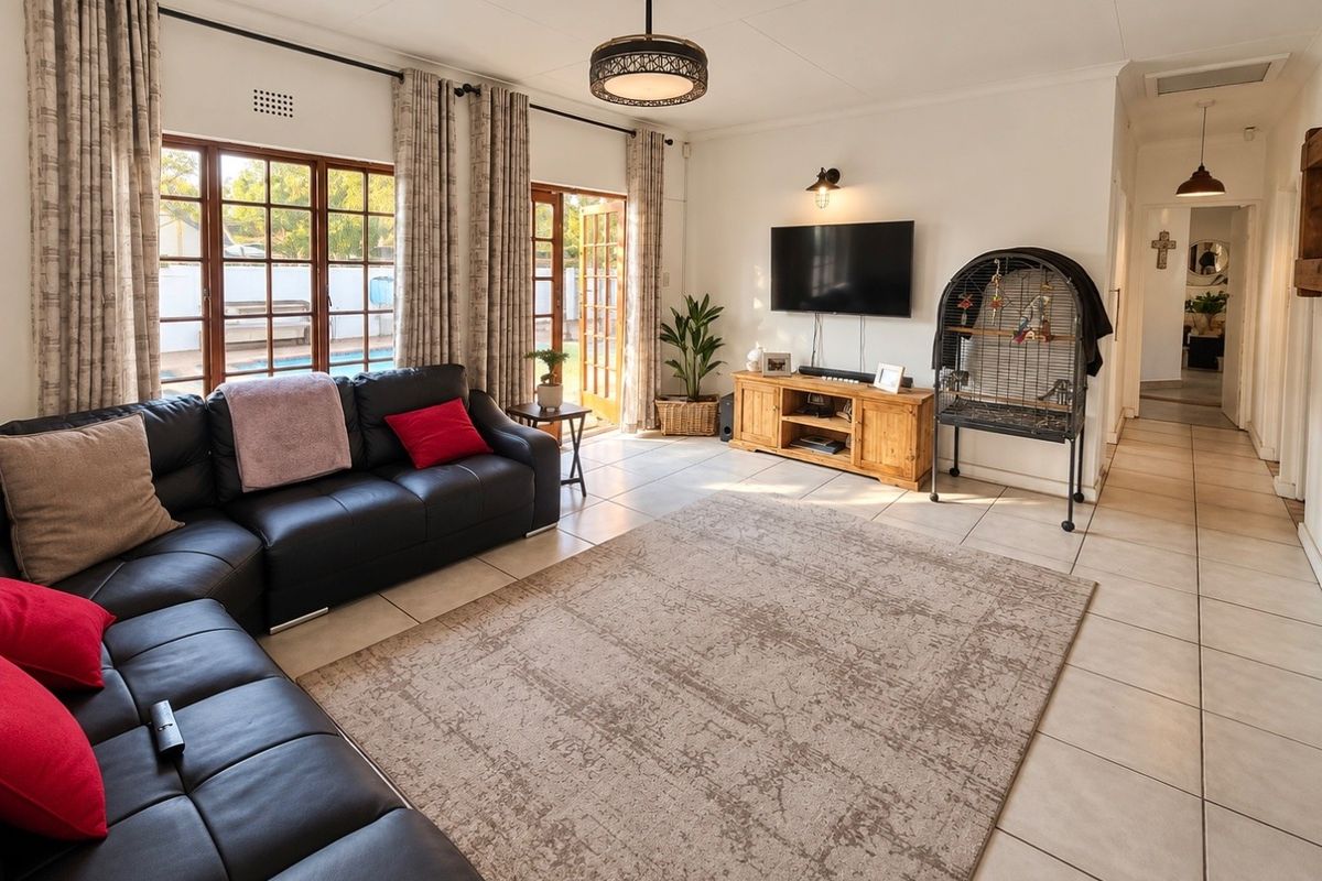 A bright and spacious living room featuring tiled flooring, large wooden-framed glass doors providing natural light, and direct access to the outdoor pool area.