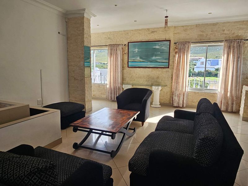 A spacious living room featuring stone-clad accent walls, tiled flooring, and large windows that provide natural light and views.