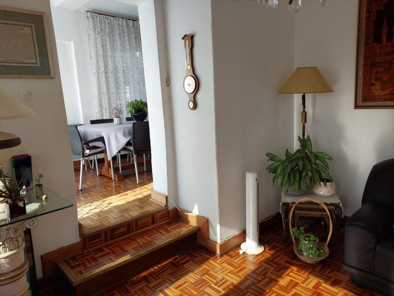 A living area featuring classic parquet flooring and a stepped transition leading into an adjacent dining space through a wide archway.