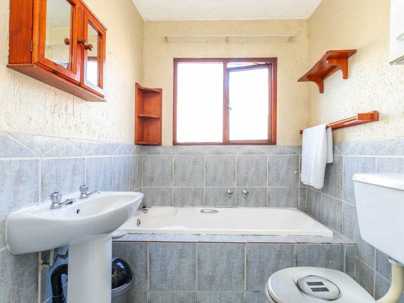 A functional bathroom featuring a pedestal basin, built-in bathtub, and tiled wall finishes, offering a classic layout with potential for modern updates.