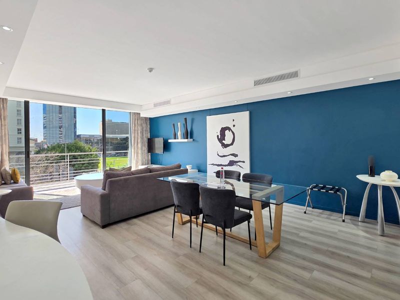 Spacious open-plan living and dining area featuring modern laminate flooring, ducted air conditioning, and large sliding doors leading to a private balcony.