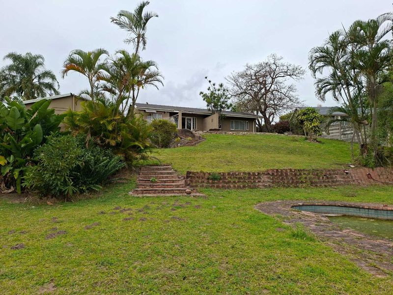 Rear view of the property featuring a large sloped garden, brick retaining walls, stairs, and an existing swimming pool.