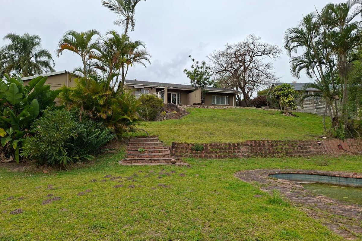 Rear view of the property featuring a large sloped garden, brick retaining walls, stairs, and an existing swimming pool.