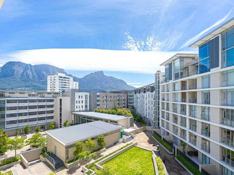 Elevated view overlooking a modern apartment complex courtyard with landscaped gardens and mountain backdrop.
