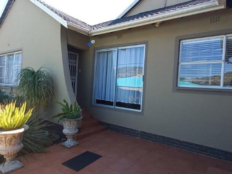 A well-maintained rear exterior view featuring a tiled patio area, sliding glass doors, and aluminium window frames under a tiled roof.