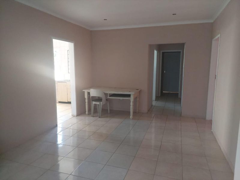 A spacious, neutrally painted living area featuring tiled flooring and recessed downlights, offering a blank canvas for interior design.