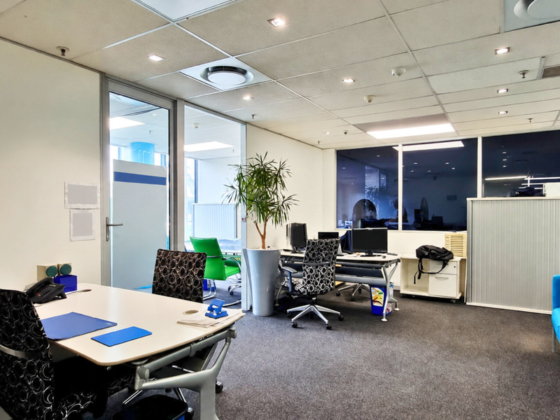 A professional office space featuring a suspended ceiling with recessed lighting, carpeted flooring, and a glass partition wall providing a bright, open work environment.