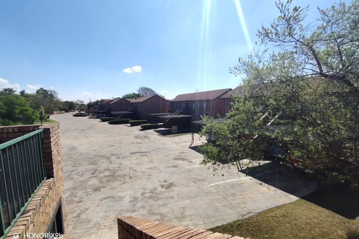 An elevated view of the townhouse complex rear area, featuring paved parking, carport structures, and established landscaping.