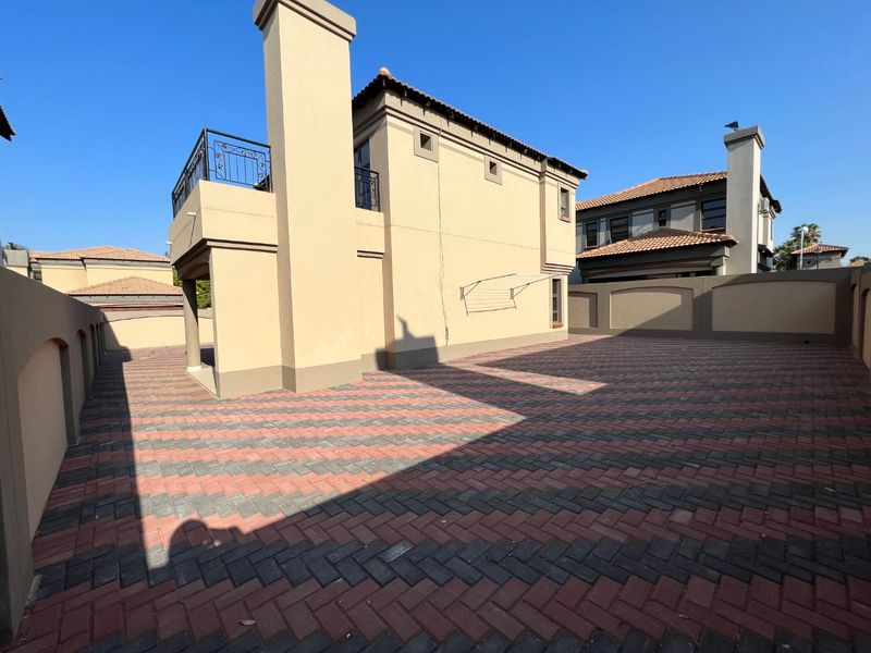 A spacious rear courtyard featuring herringbone paving, a chimney stack, and an upper-level balcony with wrought iron railings.