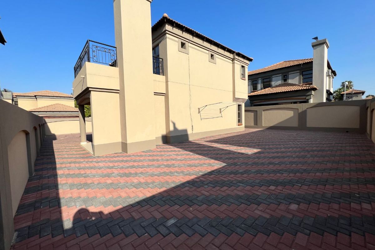 A spacious rear courtyard featuring herringbone paving, a chimney stack, and an upper-level balcony with wrought iron railings.