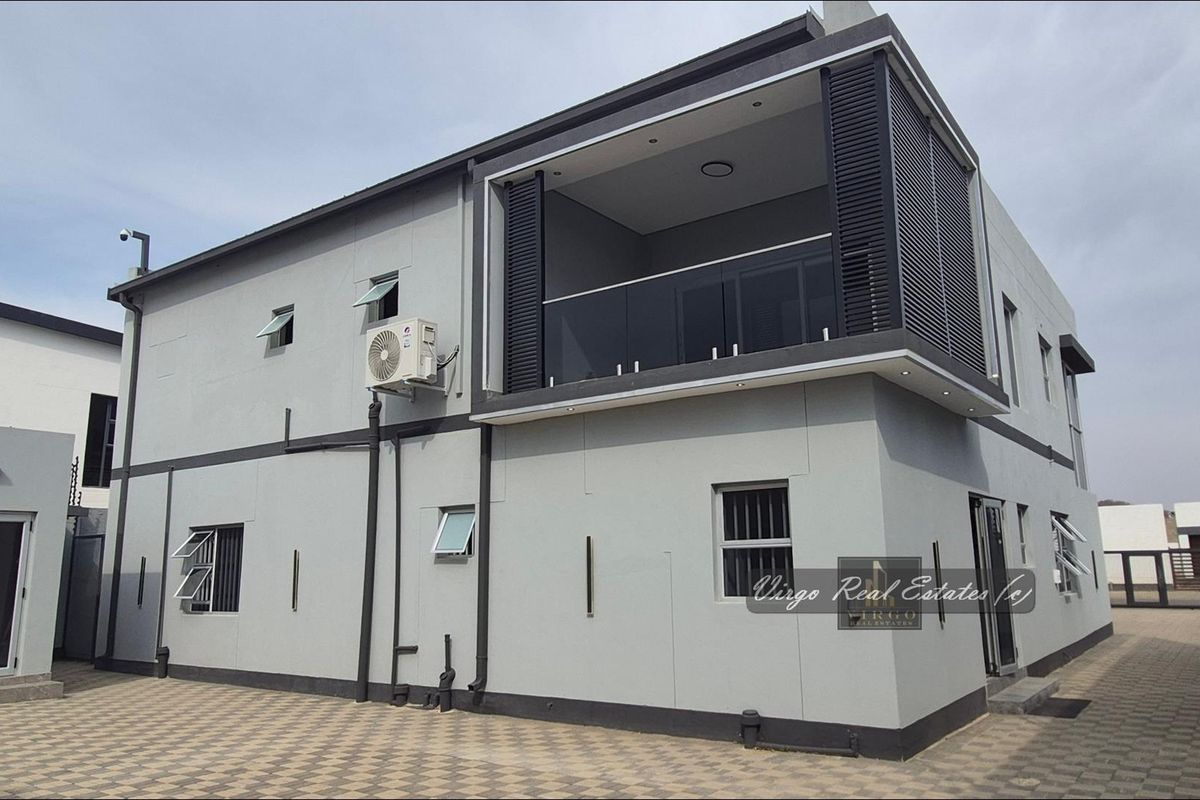 Modern two-story residential exterior featuring a balcony with glass balustrade, paved driveway, and contemporary grey facade finishes.