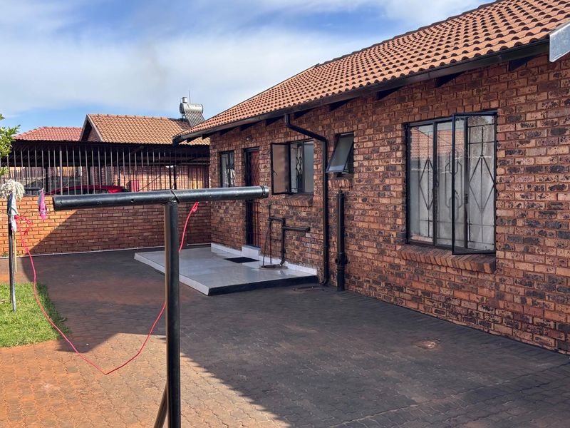 Rear exterior view of a face-brick house featuring a paved courtyard, security bars on windows, and a tiled roof.