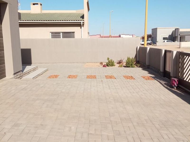 A clean, paved front driveway area featuring a secure boundary wall and sliding gate access.