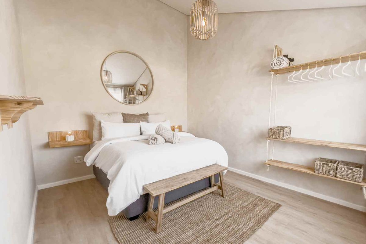 A well-maintained bedroom featuring neutral lime-wash style wall finishes, light wood-look flooring, and custom wall-mounted timber shelving units.