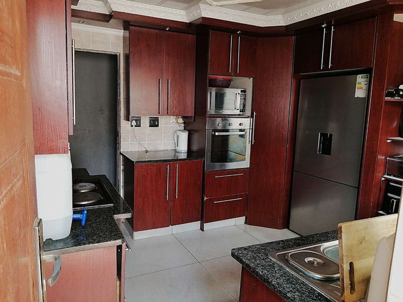 A functional kitchen featuring dark wood cabinetry, granite countertops, built-in oven and microwave, and tiled flooring.