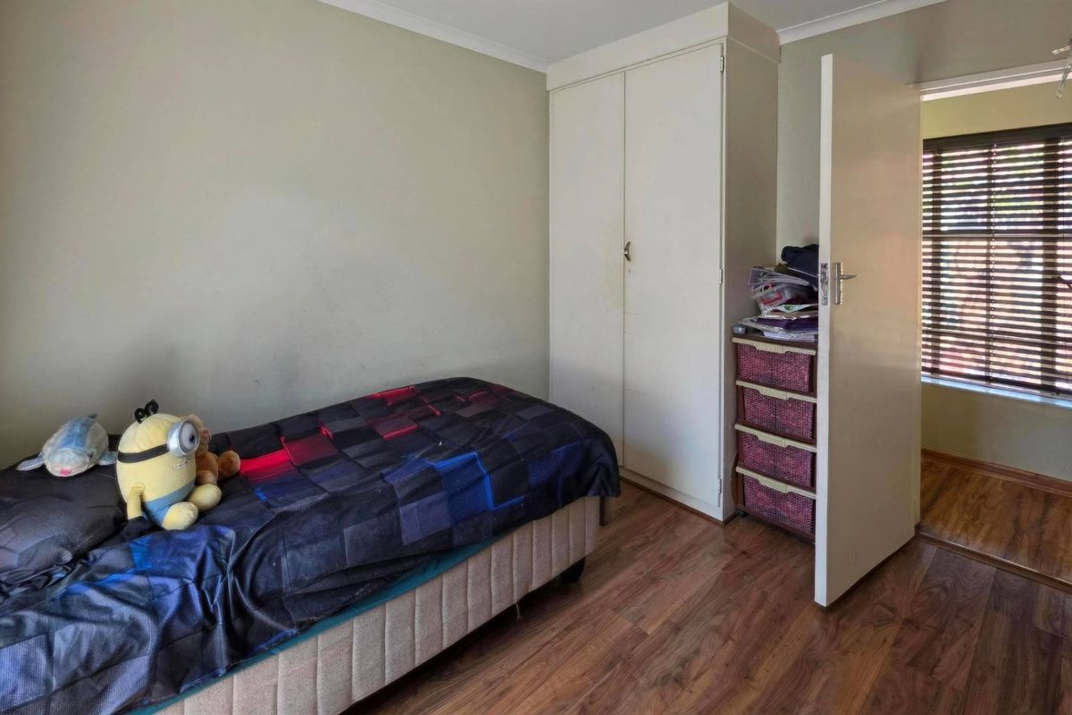 A bedroom featuring laminate flooring, a built-in wardrobe, and venetian blinds, offering a functional space with potential for cosmetic updates.