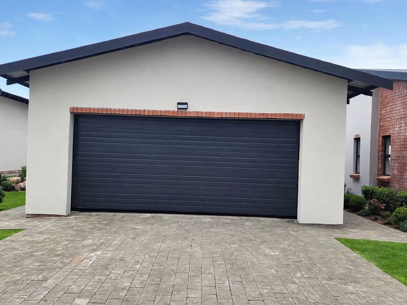 A well-maintained single garage featuring a modern dark sectional door, paved driveway, and clean exterior finishes.