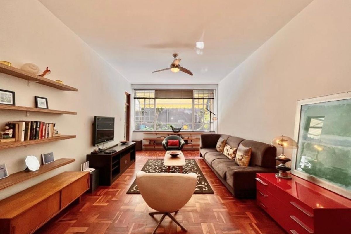 A well-maintained living room featuring classic parquet timber flooring, built-in wall shelving, and a large window providing natural light.