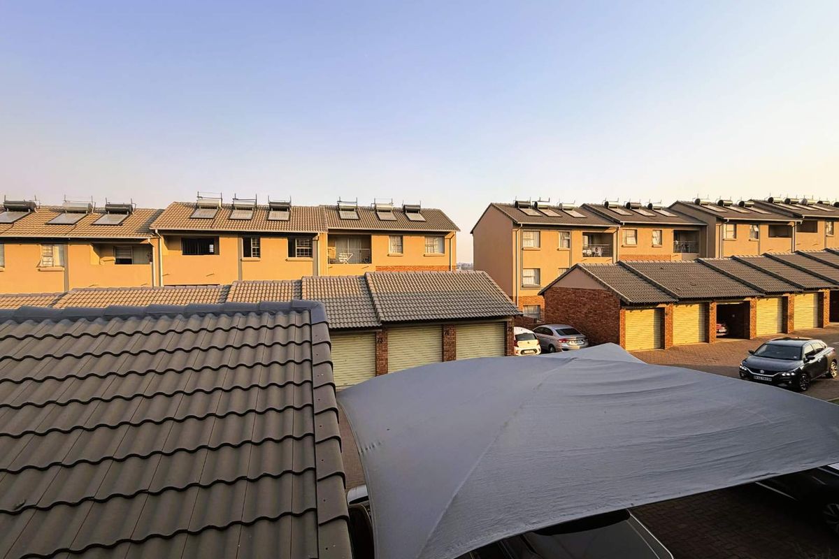 An elevated view of a residential apartment complex featuring multiple units with tiled roofs, solar water heating systems, and a paved parking area.
