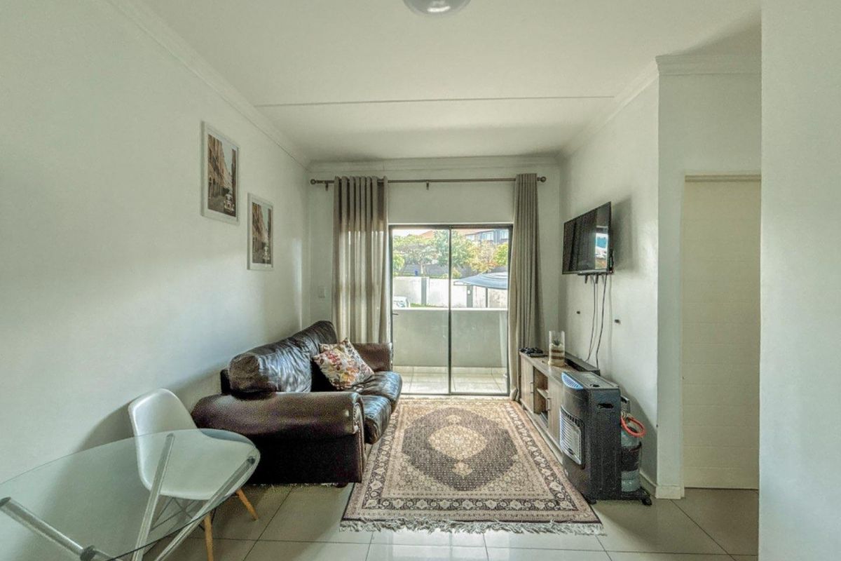 A compact living area featuring tiled flooring, a sliding glass door leading to a balcony, and neutral wall finishes.
