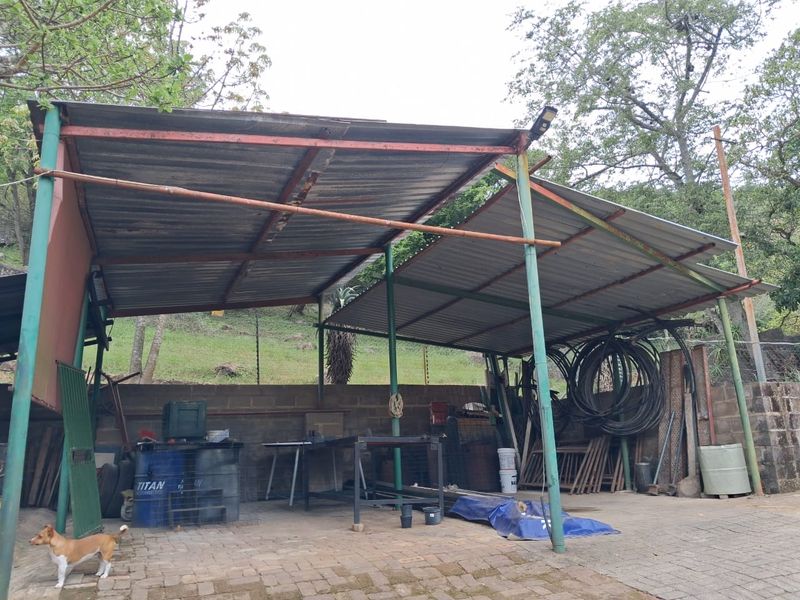An outdoor utility or workshop area featuring a corrugated metal roof structure supported by steel columns and paved flooring.