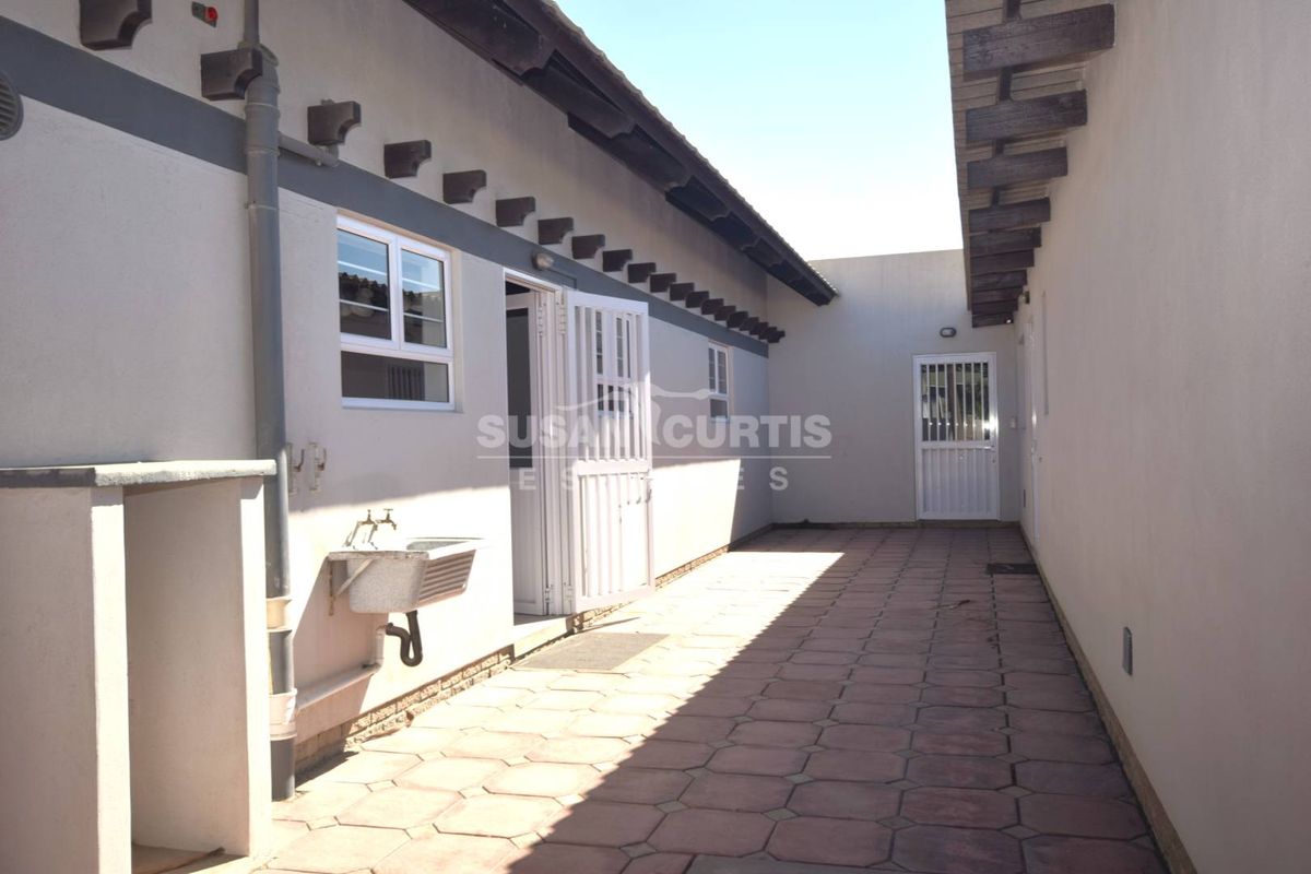 A paved rear courtyard area featuring an external utility sink, security gates, and exposed rafter detailing along the building exterior.