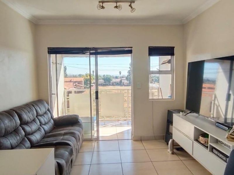 A living room featuring tiled flooring, coving, and a sliding glass door that provides access to a balcony with exterior views.