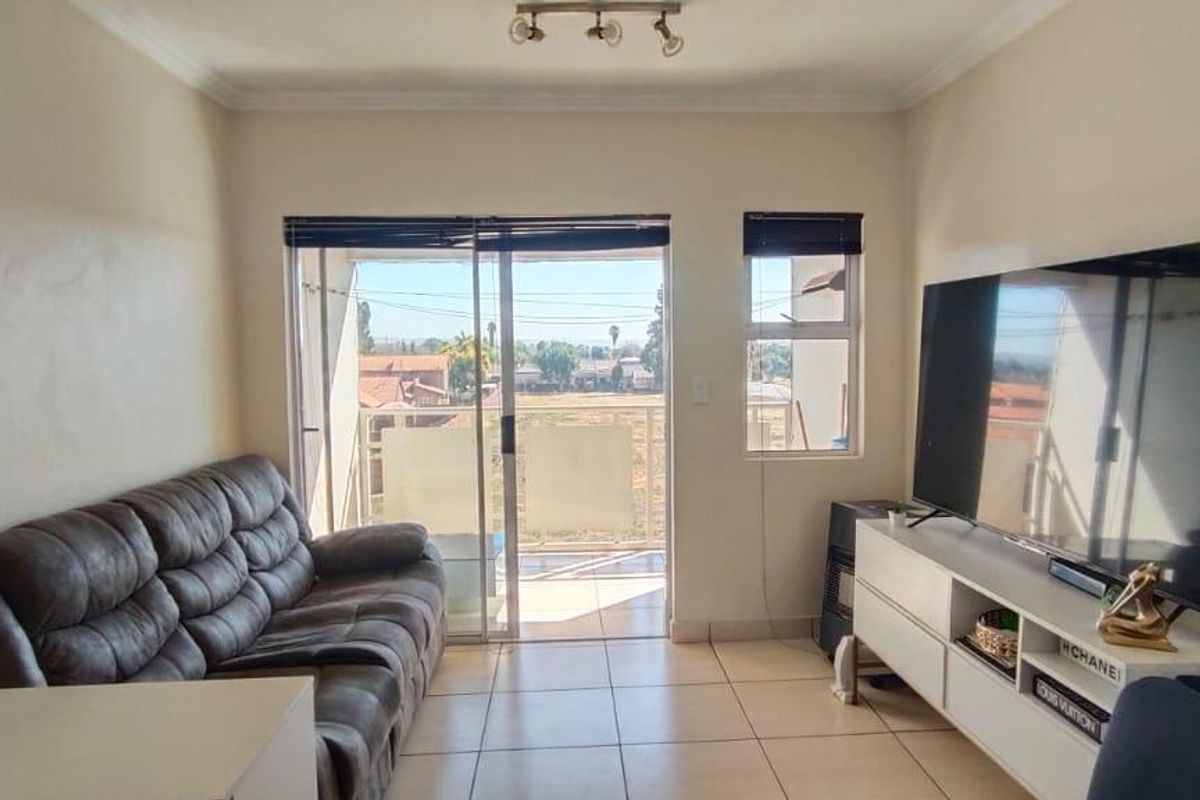 A living room featuring tiled flooring, coving, and a sliding glass door that provides access to a balcony with exterior views.