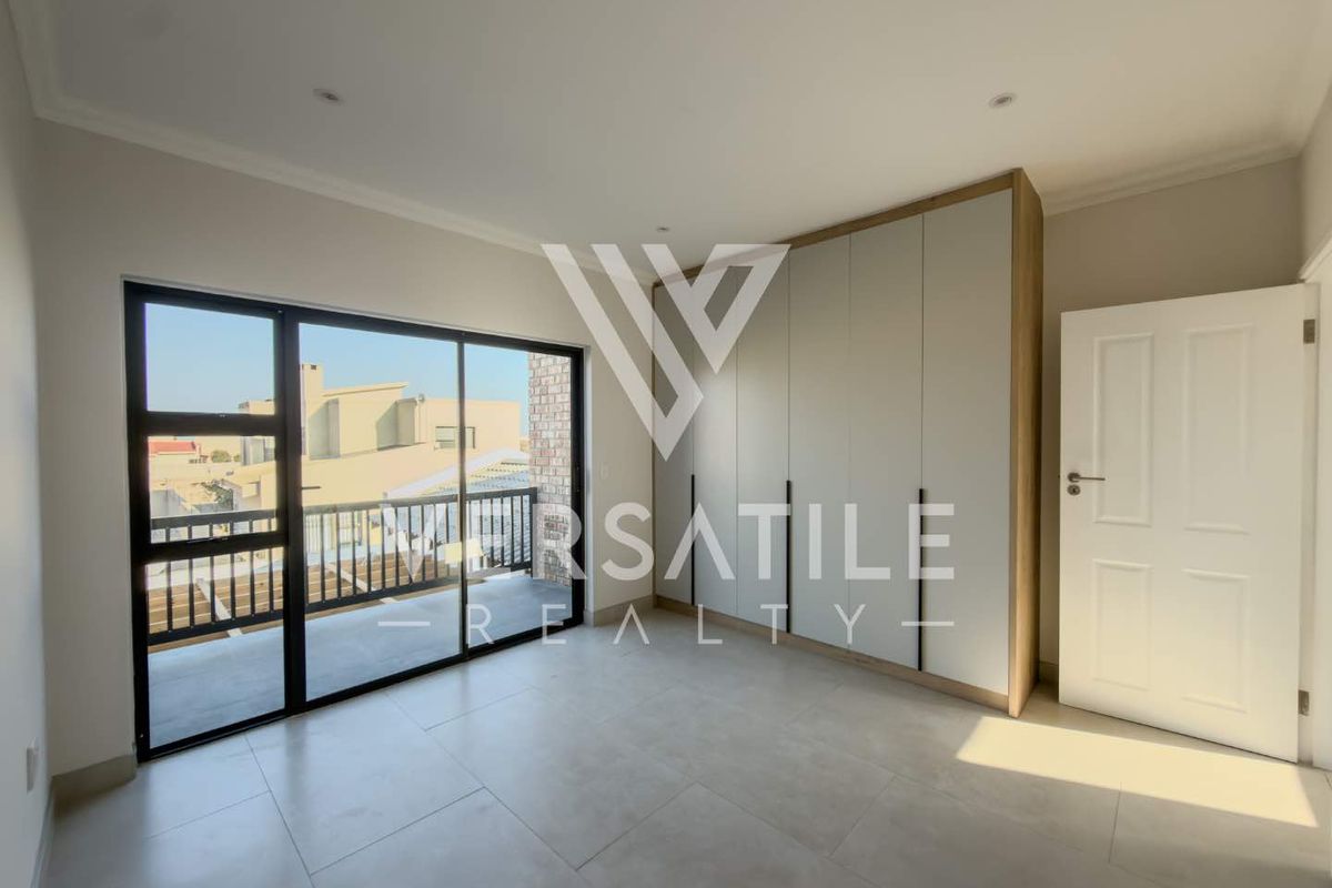 A bright, modern bedroom featuring neutral tiled flooring, floor-to-ceiling built-in cupboards, and a sliding glass door leading to a private balcony.