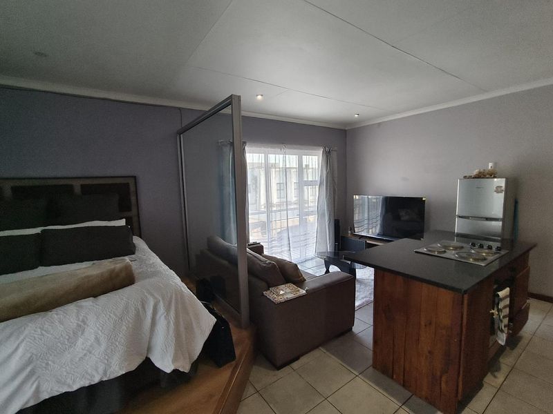 Open-plan studio apartment featuring a kitchen island with electric hob, glass room divider, and direct access to a balcony through sliding glass doors.