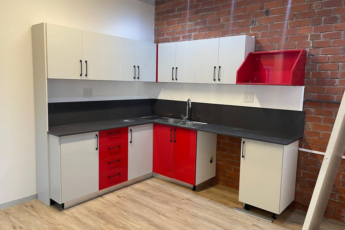 A modern kitchenette featuring high-contrast red and white cabinetry, dark countertops, a stainless steel sink, and an industrial-style exposed brick feature wall.