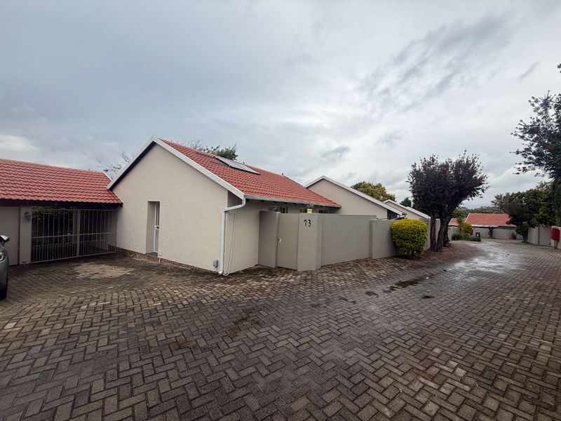 Front exterior view of a townhouse featuring a paved driveway, tiled roof, and secure boundary wall with gated access.