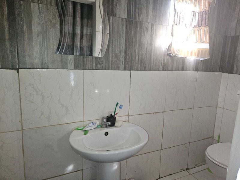 A compact bathroom featuring a pedestal washbasin and wall tiling. The space shows signs of wear and requires maintenance on the tile finishes.