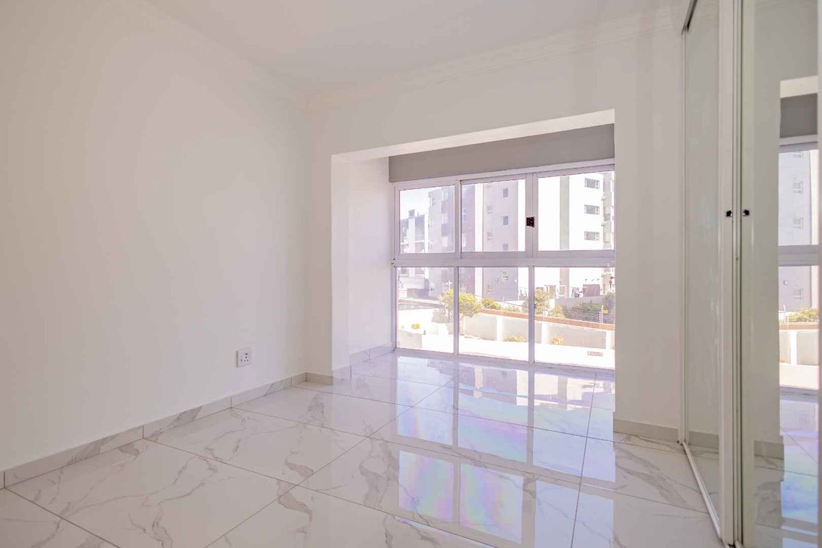 A bright, empty bedroom featuring modern marble-look porcelain floor tiles, a built-in sliding door wardrobe, and large windows providing ample natural light.