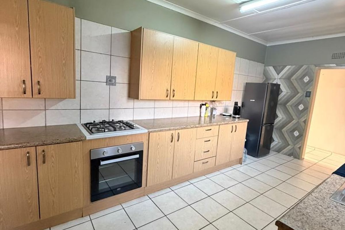 A functional kitchen featuring light wood cabinetry, granite countertops, a gas hob, built-in oven, and tiled flooring throughout.