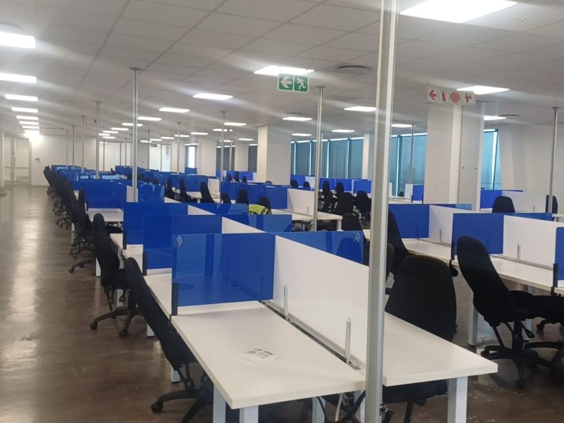 A spacious open-plan office area featuring polished concrete floors, suspended ceilings with recessed lighting, and large windows providing ample natural light.
