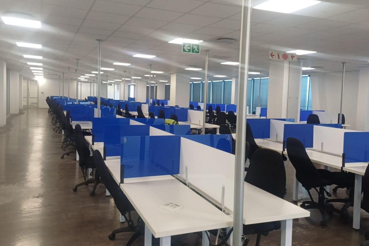 A spacious open-plan office area featuring polished concrete floors, suspended ceilings with recessed lighting, and large windows providing ample natural light.