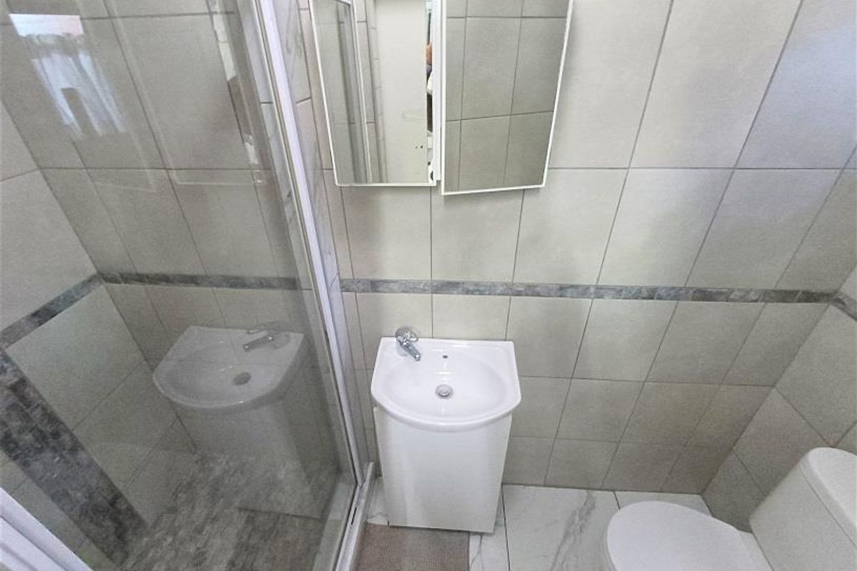 A compact, modern bathroom featuring a glass shower enclosure, pedestal basin, toilet, and neutral wall tiling with marble-effect flooring.