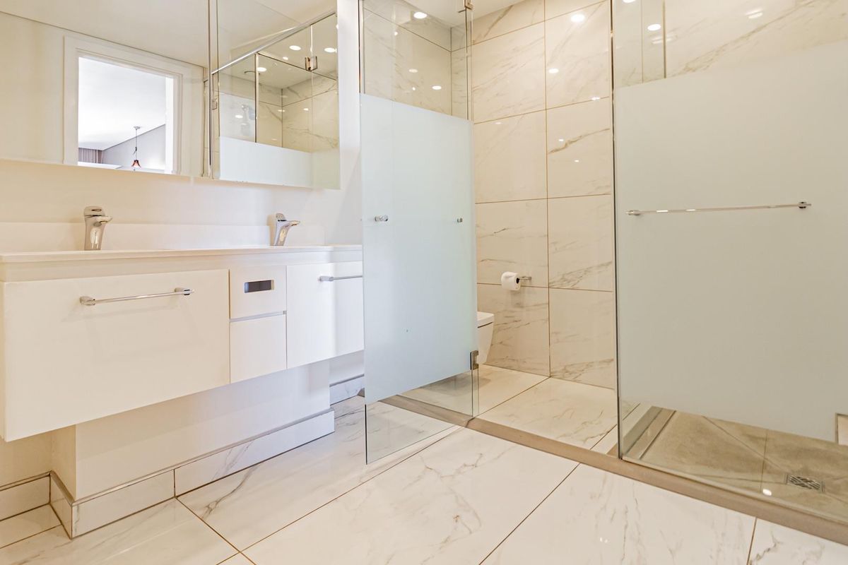 Modern bathroom featuring a floating double vanity, marble-look floor and wall tiles, and a spacious walk-in glass shower enclosure.