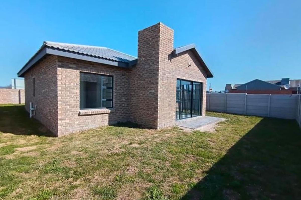 Rear view of a face brick house featuring a chimney, sliding glass doors, and a private garden enclosed by a precast concrete boundary wall.